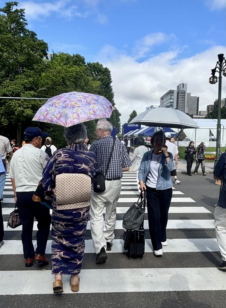 横断歩道を渡る人たちの中で日傘をさす女性