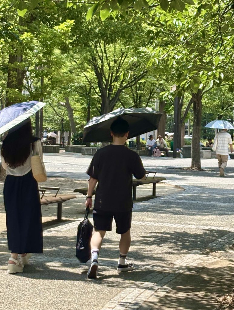 並木道で日傘を斜めに傾けてさして歩く人