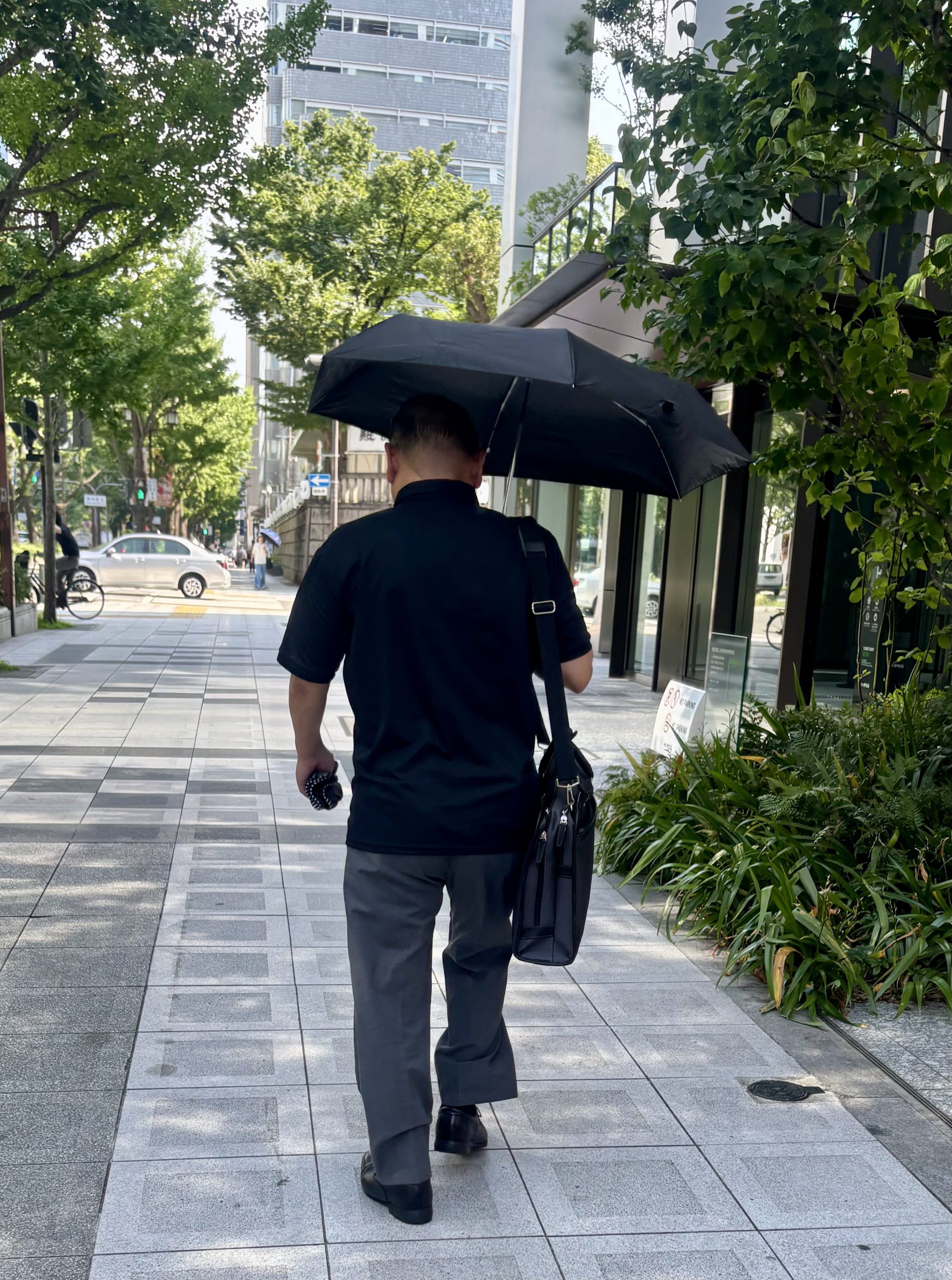 通勤中に折りたたみ日傘をさす男性